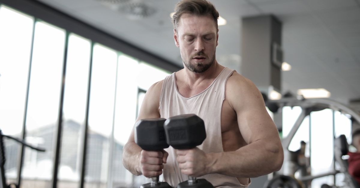 Strong man lifting dumbbells for muscle building in a modern gym setting.