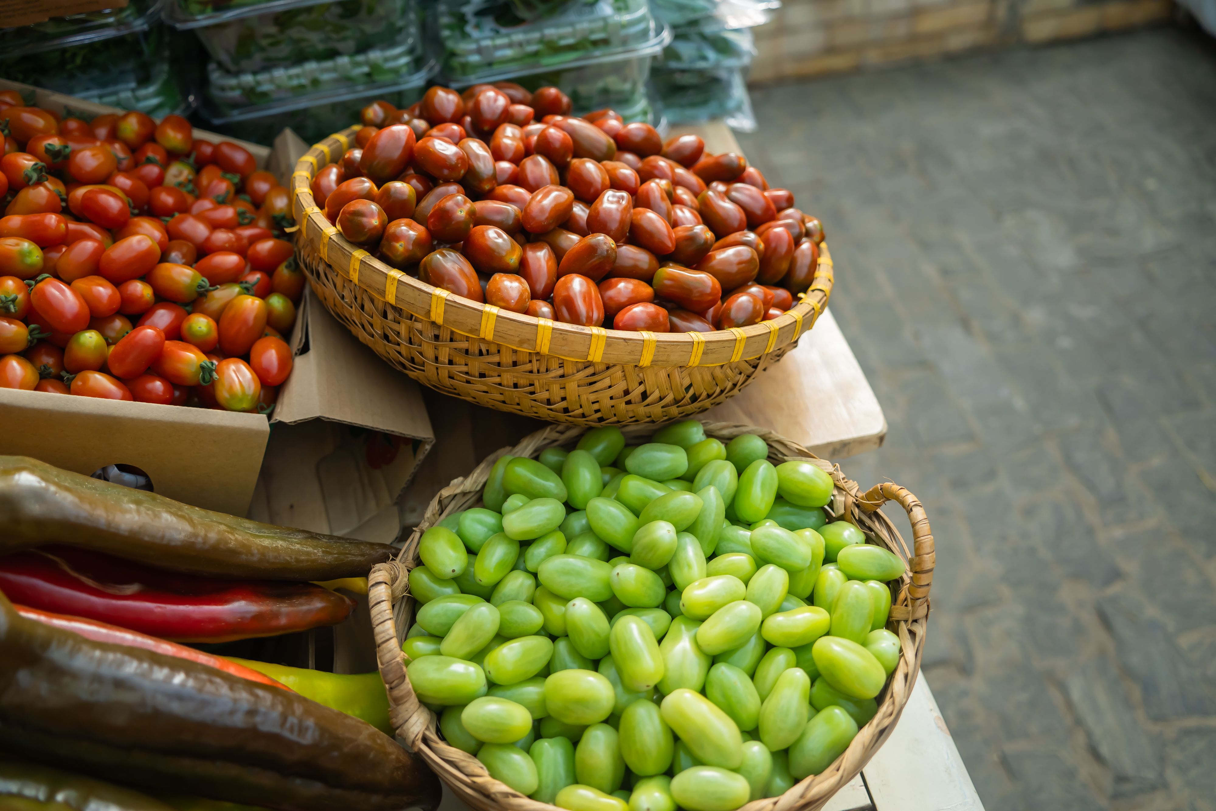 Vibrant fresh vegetables including tomatoes and peppers arranged in baskets at a market stall.
