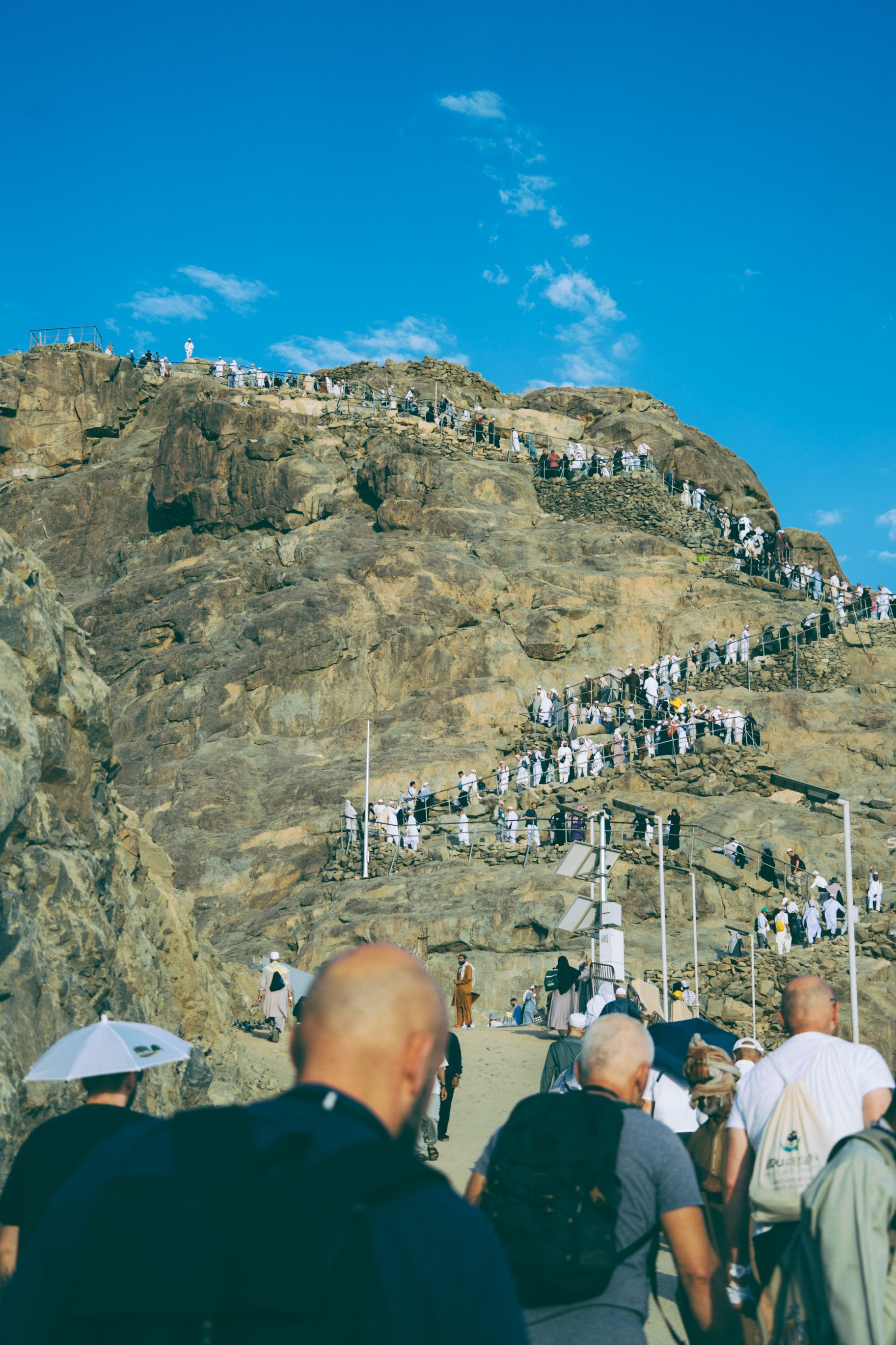 Pilgrims climbing the sacred mountain Jabal al-Noor in Makkah, Saudi Arabia, under a clear blue sky.
