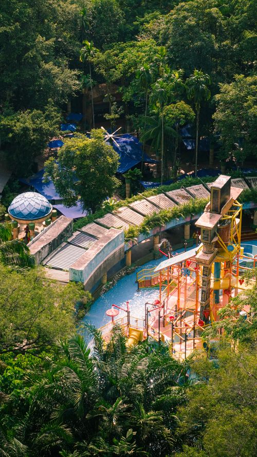 Free A secluded water park nestled in dense tropical vegetation viewed from above, showcasing colorful slides and structures. Stock Photo
