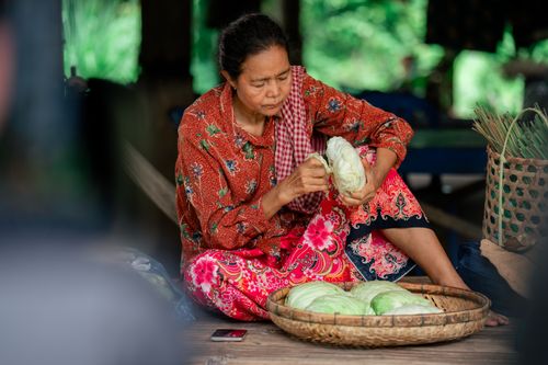 Free A woman sits indoors peeling cabbage, showcasing traditional lifestyle and attire. Stock Photo