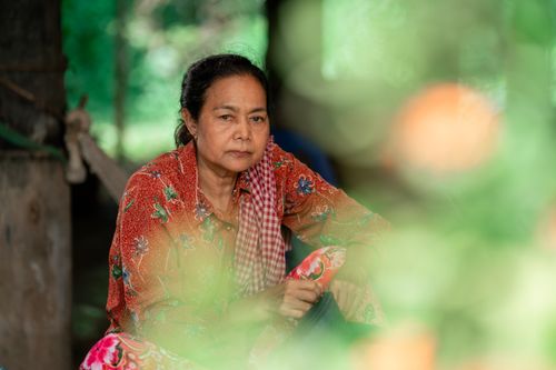 Free Portrait of a woman in colorful attire sitting thoughtfully indoors with a blurred foreground. Stock Photo