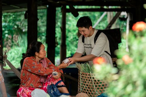 Free Smiling man shares smartphone with local woman in an outdoor village setting, embracing cultural exchange. Stock Photo