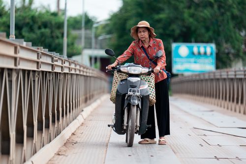 Free A woman in traditional attire rides a motorcycle across a bridge. Stock Photo