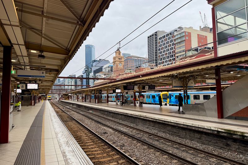 A view of Flinders Street Station platforms in Melbourne with trains and commuters under a cloudy sky.