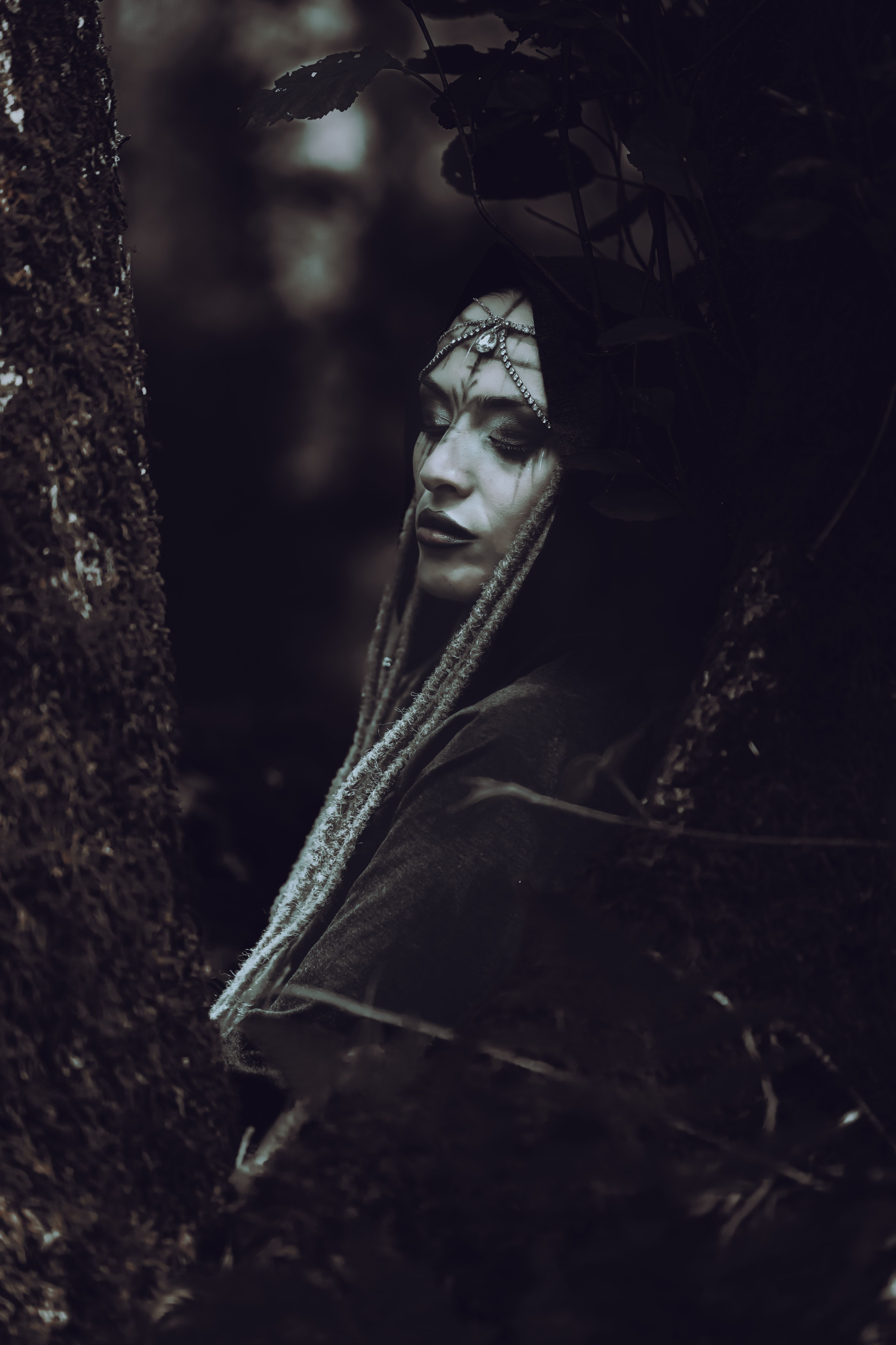 Mysterious woman with decorative headpiece in a dark, moody forest scene, evoking fantasy themes.
