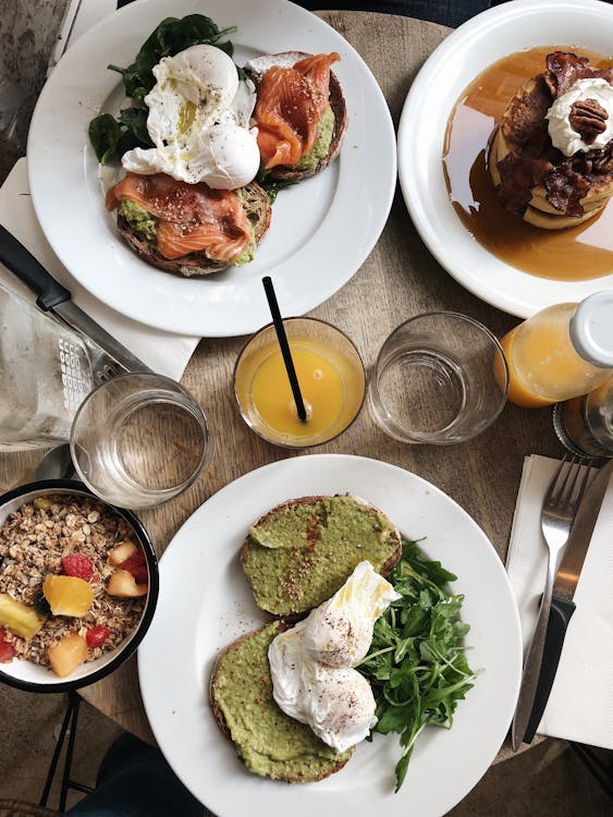 Free Top view of plates of assorted healthy toasts with poached eggs and natural juice served on wooden table near oatmeal bowl and sweet pancakes Stock Photo