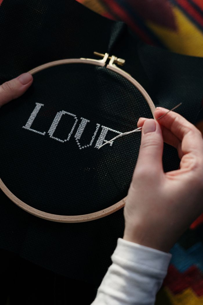 Hands stitching the word LOVE on black fabric in a hoop