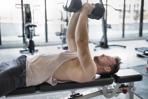 Free Active man engaged in strength training with dumbbells in a modern gym setting. Stock Photo