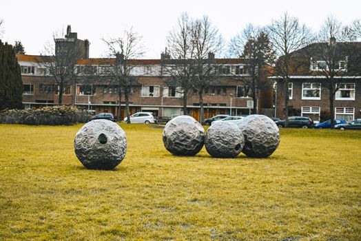 Sculptural stone spheres set in a grassy urban park with brick buildings.