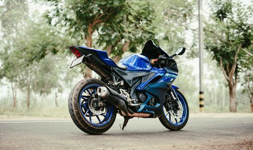 Free A stunning blue motorcycle parked on a scenic road, showcasing its sleek design against a green tree backdrop. Stock Photo