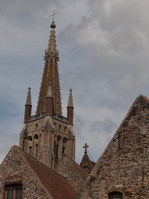 Free Detailed view of a Gothic church spire dominating the skyline in Bruges, Belgium under a cloudy sky. Stock Photo
