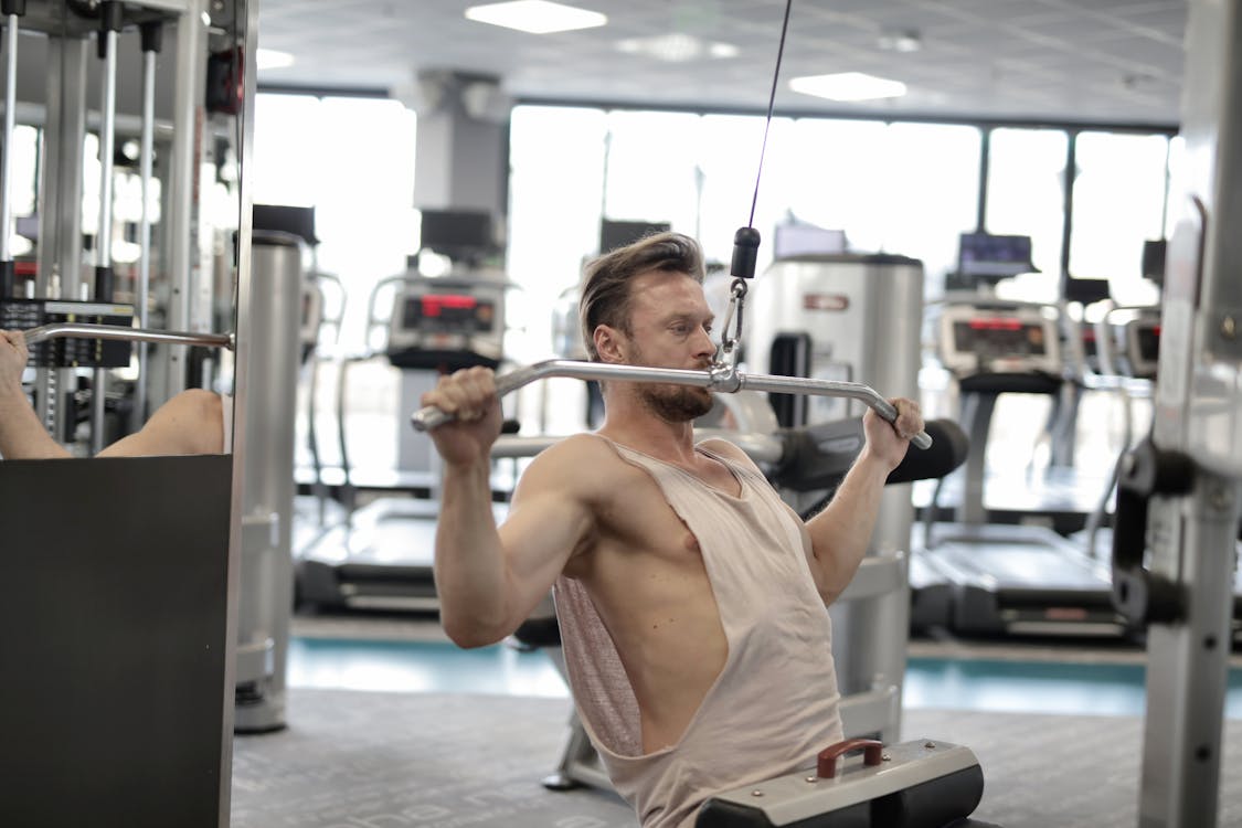 Free Powerful muscular male athlete in casual sportswear performing exercise with metal bar on machine while training hard in modern fitness club Stock Photo