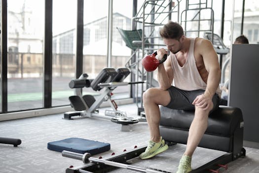 Young man performing bicep curls with kettlebell in a well-equipped gym.