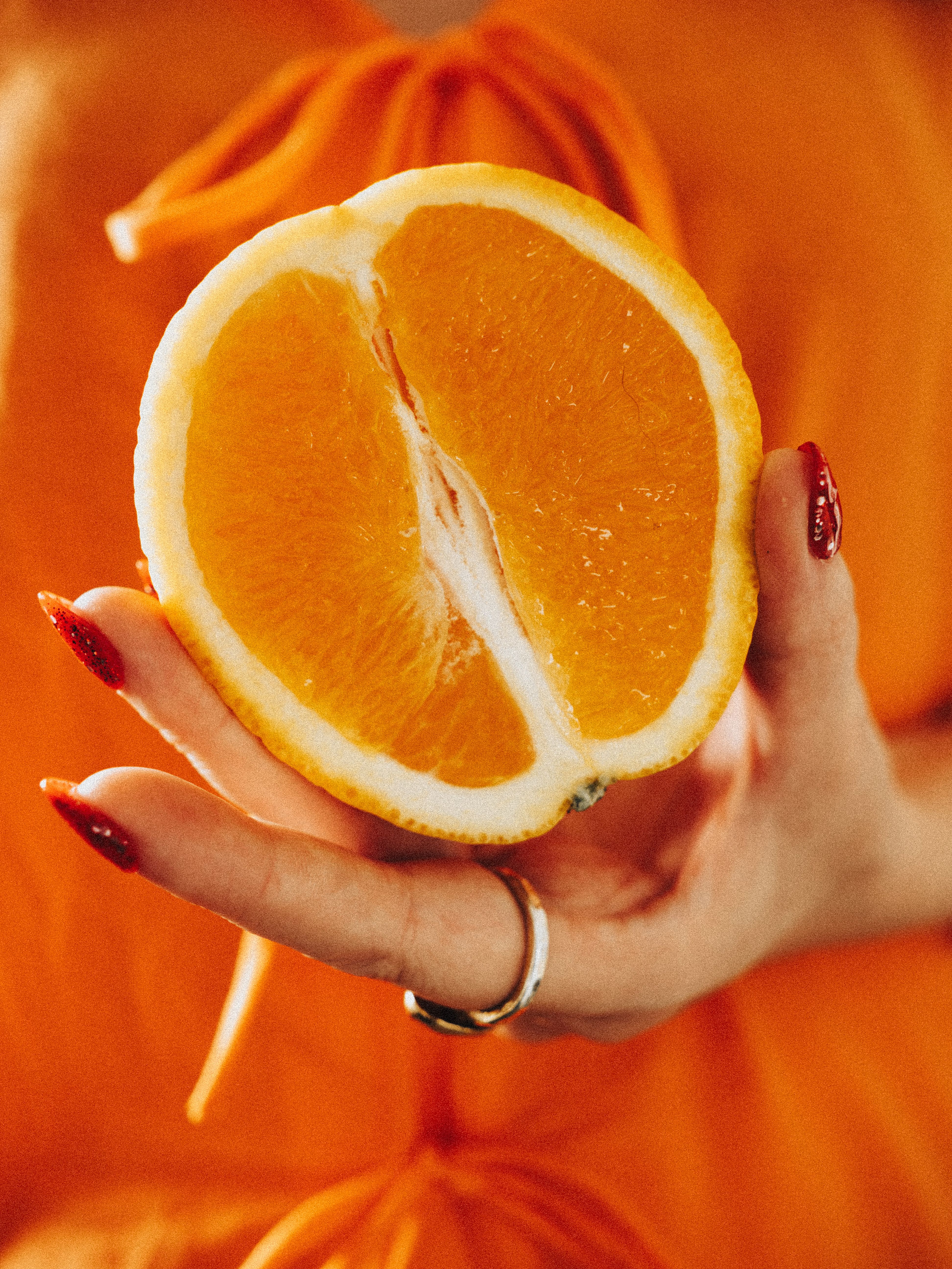 Close-up of a sliced orange half held in hand against an orange backdrop.