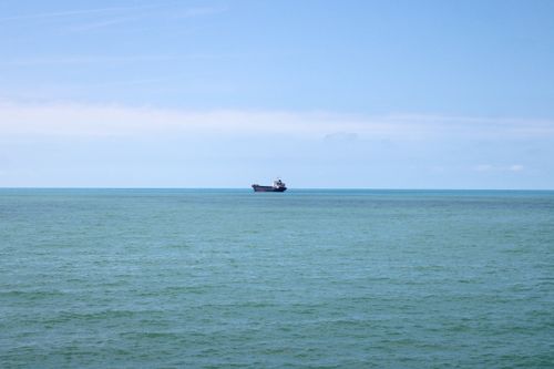 Free A solitary cargo ship travels across a calm, expansive ocean under a clear blue sky. Stock Photo