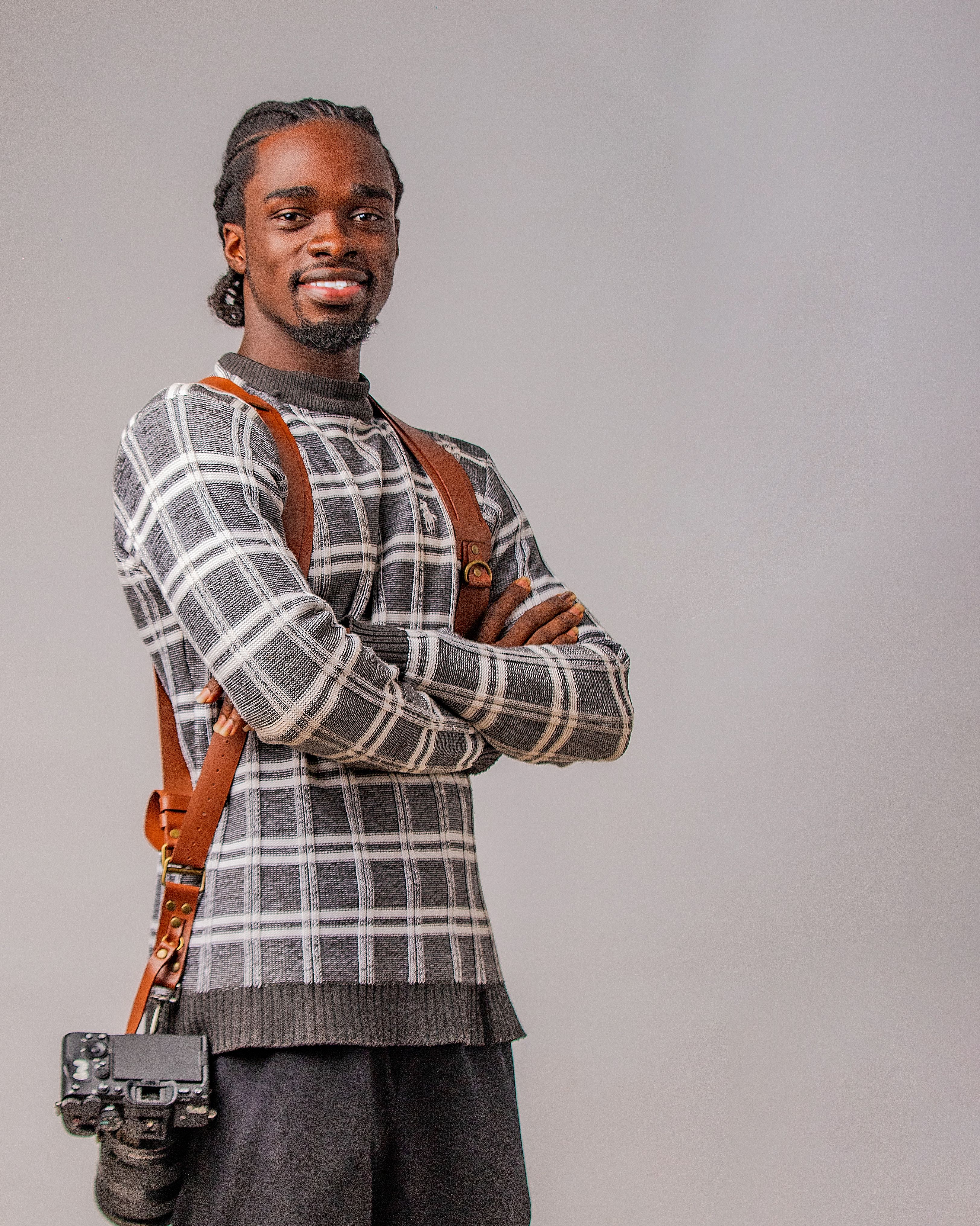 Smiling photographer with camera and leather harness against gray background.