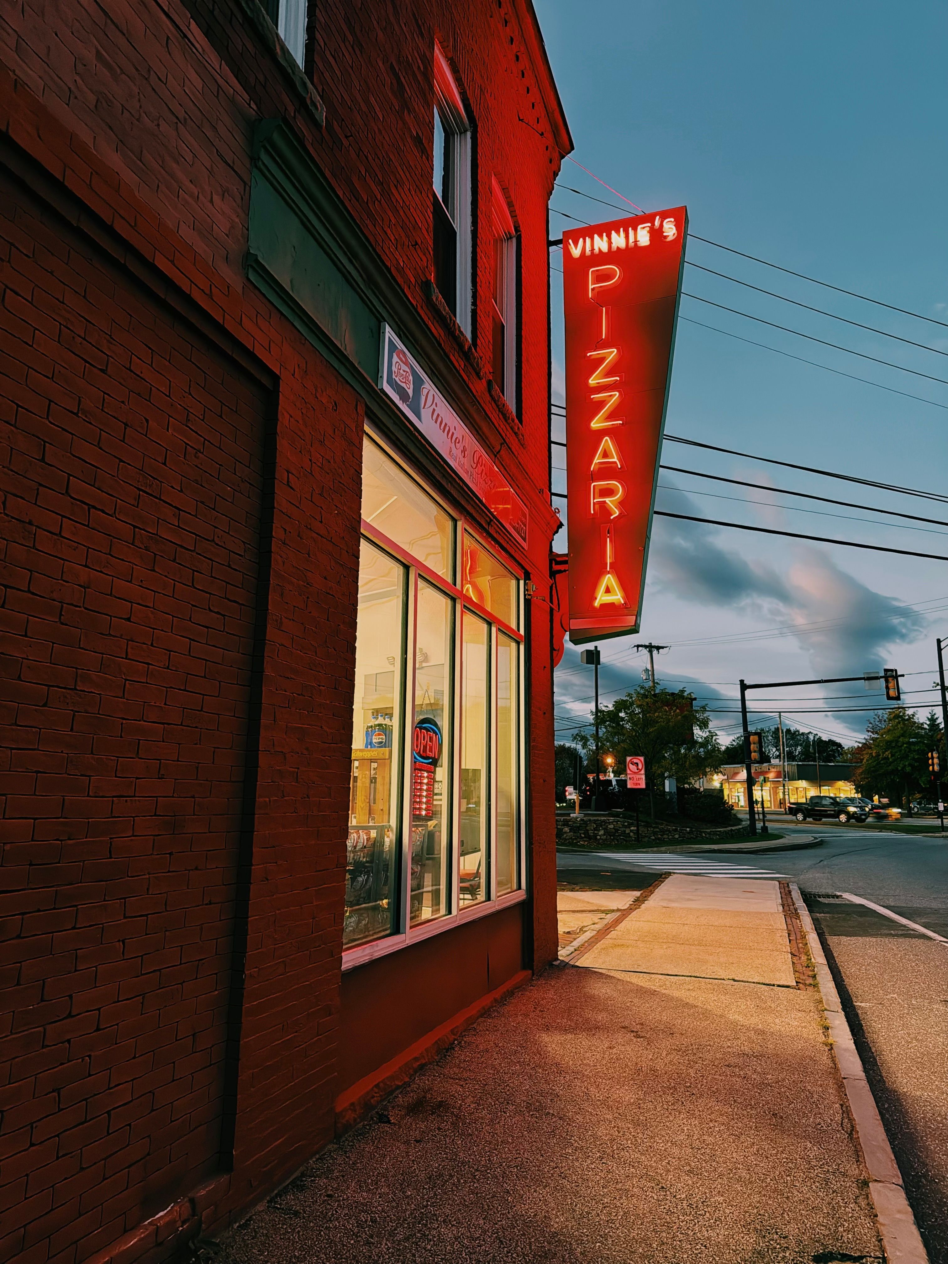 Vibrant neon sign of Vinnie's Pizzaria glowing at dusk. Captured beautifully with a retro vibe.