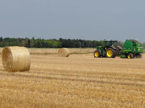 A green tractor baling straw outdoors in a field near Neuss, Germany.