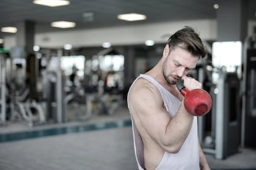 Man in White Tank Top Holding Red Kettlebell