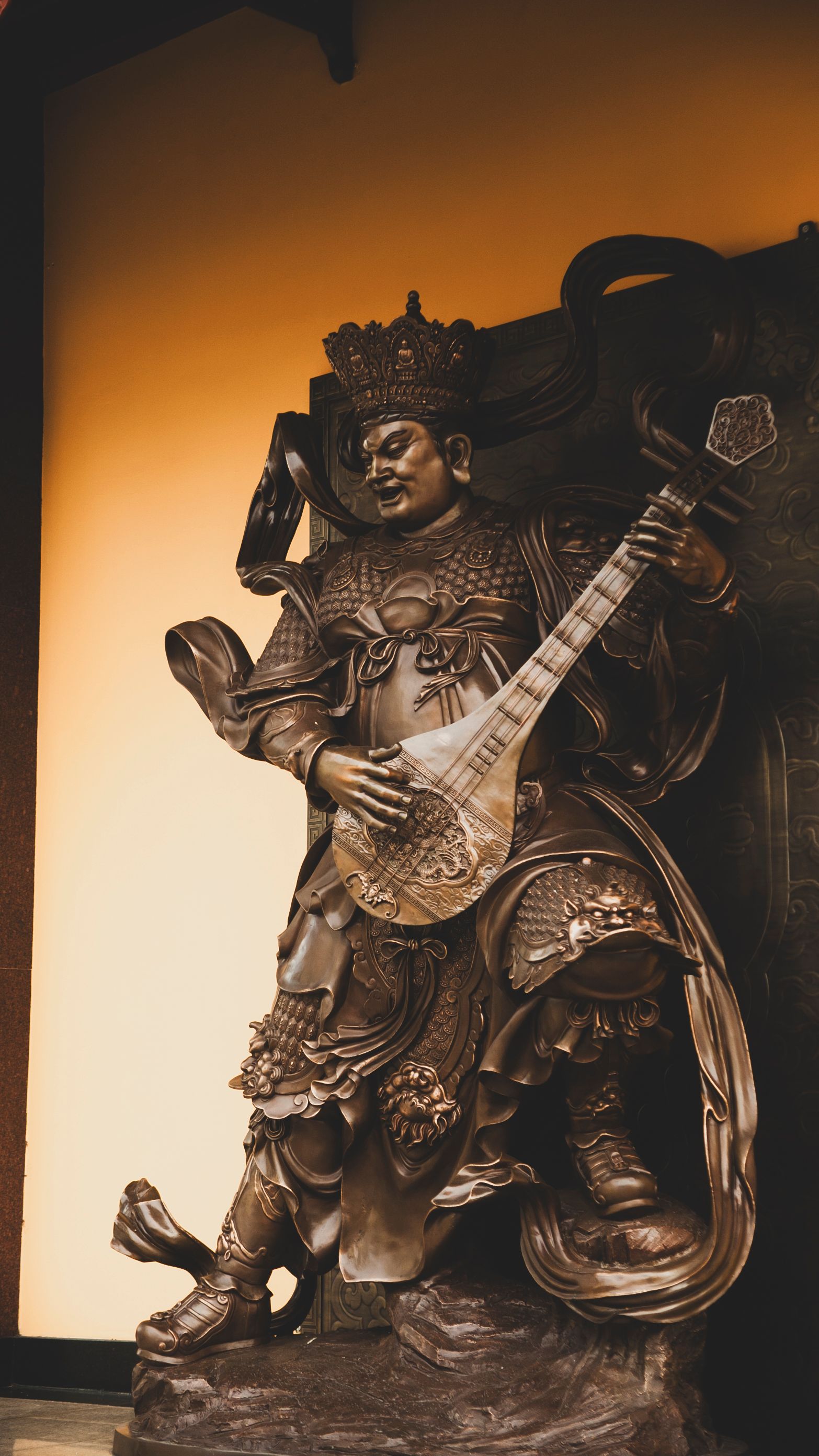 Bronze statue of a warrior deity playing a lute, symbolizing protection and music in Eastern culture.