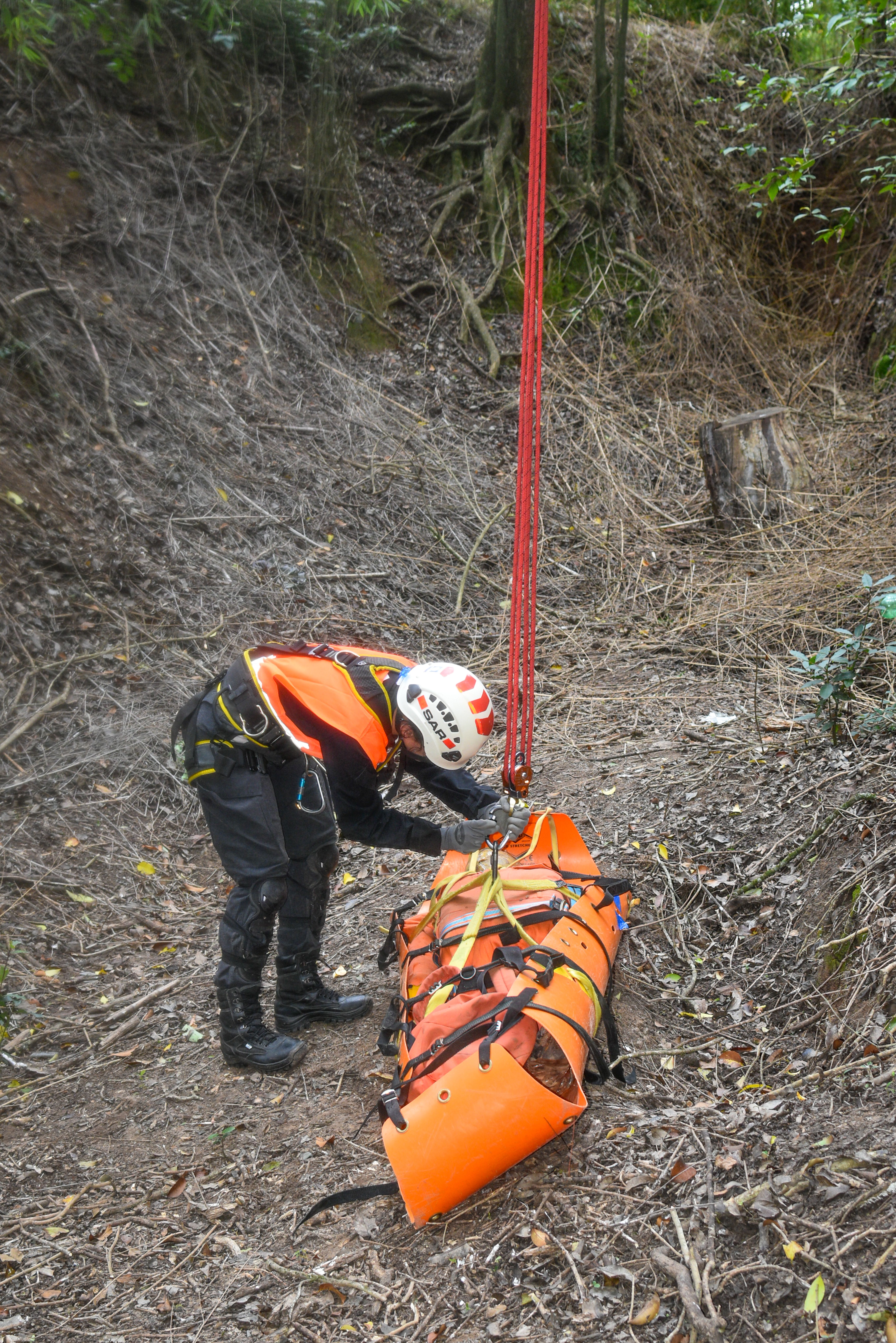 A rescue worker secures a stretcher during an operation in a forested area.