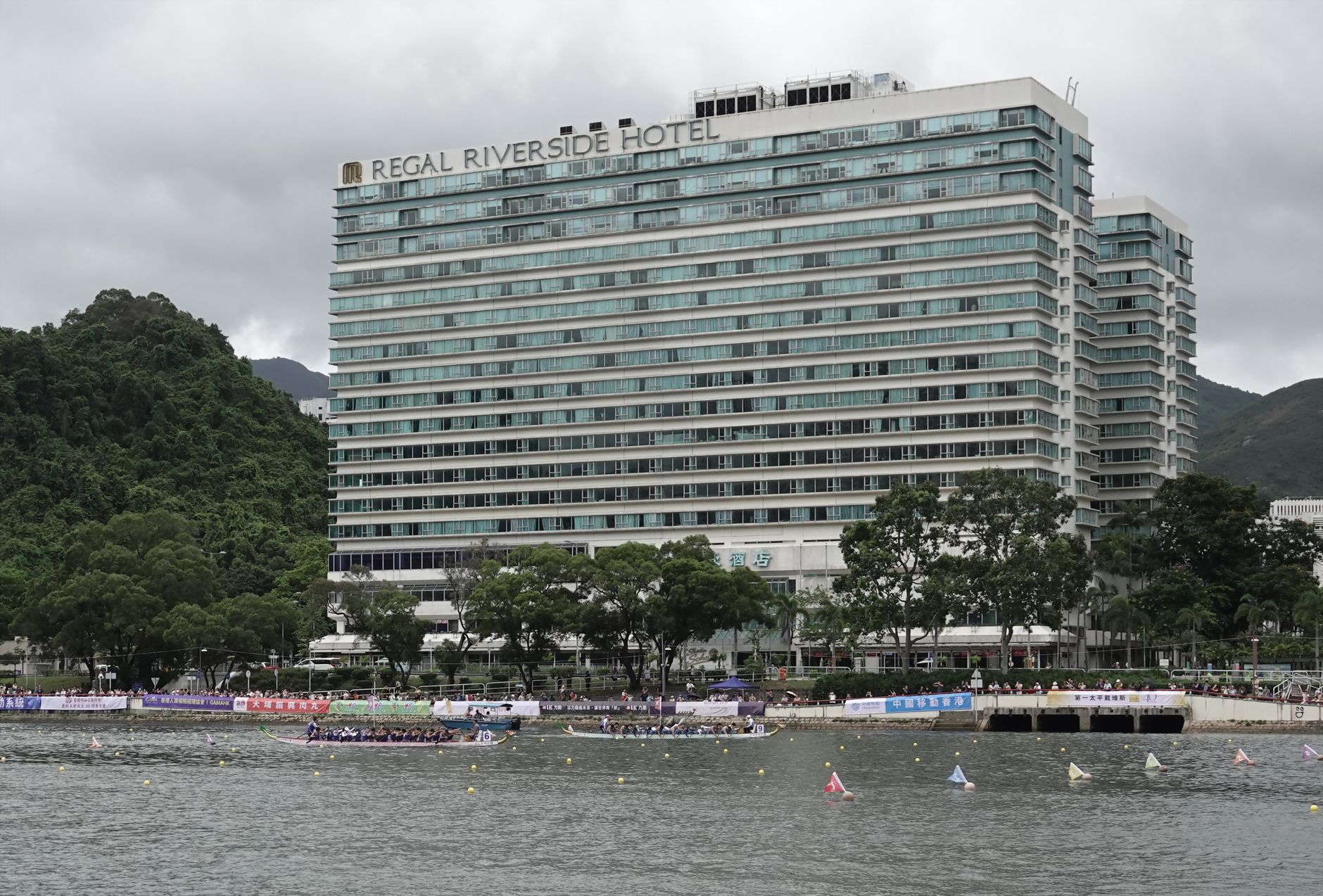 Panoramic view of Regal Riverside Hotel with a dragon boat race on the Shing Mun River in Hong Kong.