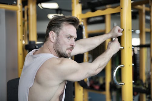 Serious muscular male athlete training near exercise machine in fitness center