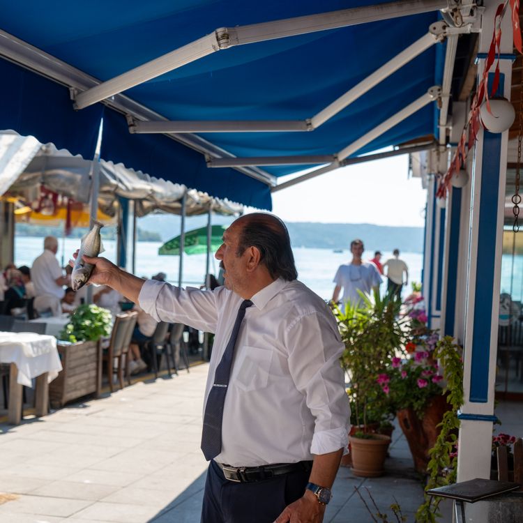 Konobar poslužuje svježu ribu u restoranu uz more s plavim tendama