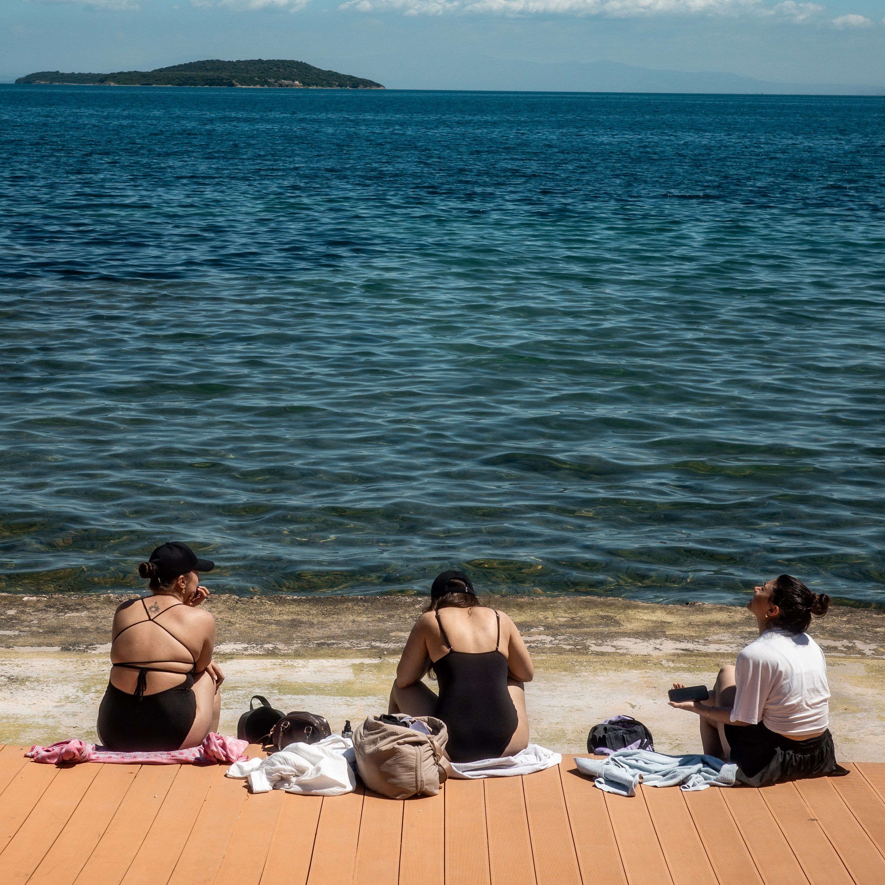 Three women sit by the sea on a sunny day, enjoying the view and leisure time.