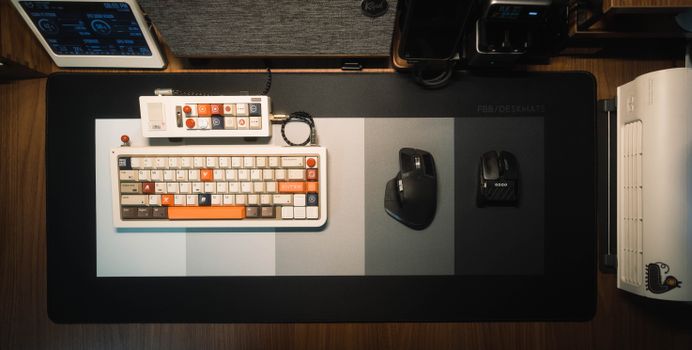 Top view of a neat and stylish minimalist workspace featuring a custom keyboard, two mice, and assorted gadgets on a desk mat.