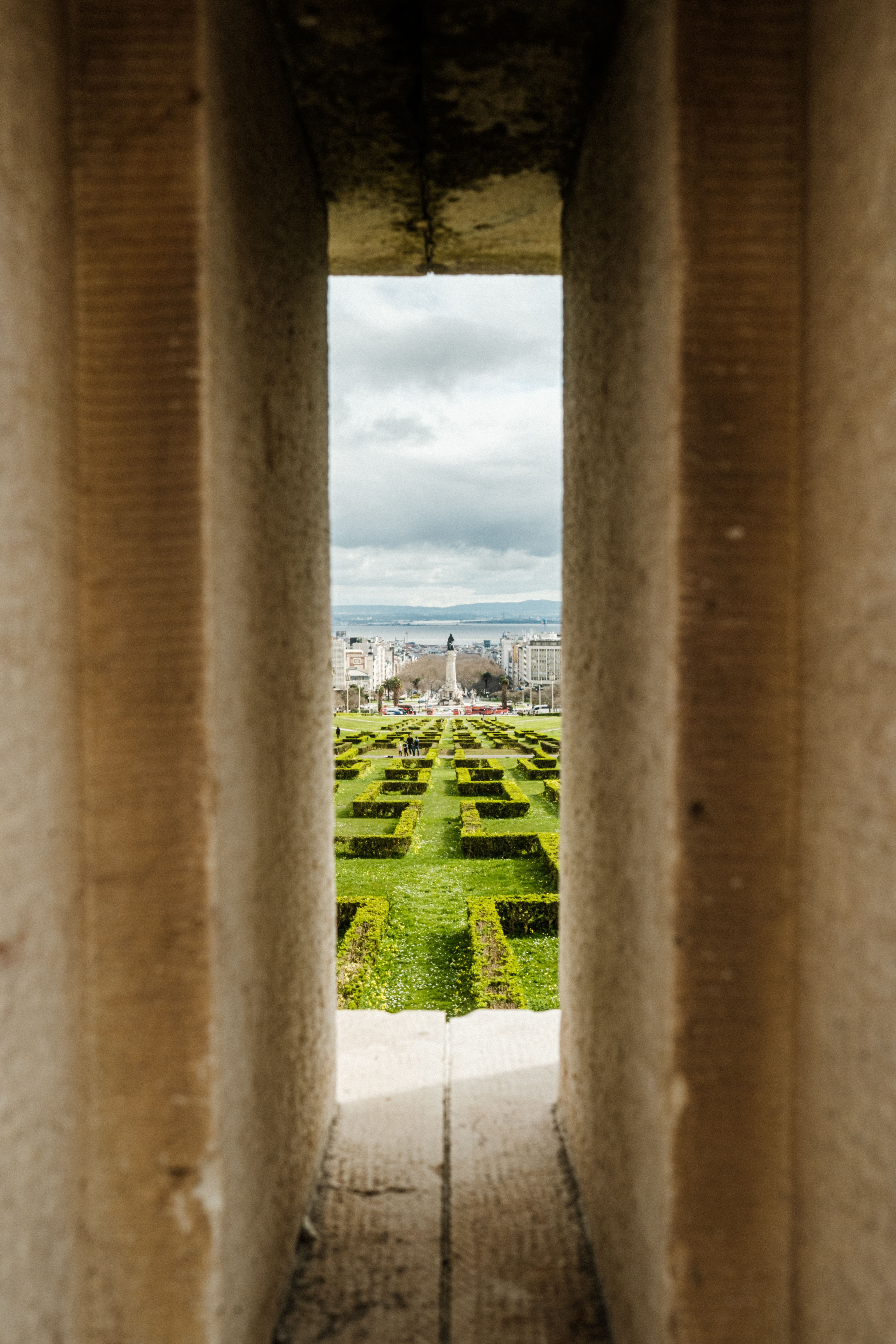 A garden with geometric hedges framed by a stone archway, capturing an architectural view.