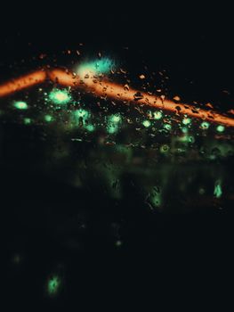 Abstract view of raindrops on a window with colorful bokeh lights in the background.