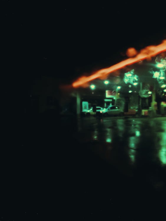 Defocused cars on gas station with neon illumination at night in rainy weather