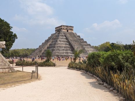 View of El Castillo Pyramid at Chichen Itza, Yucatan, Mexico with tourists exploring the historic site.