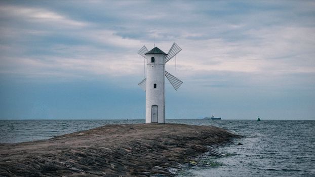 Lighthouse-shaped windmill beacon on a coastal breakwater at dawn, offering navigational aid.
