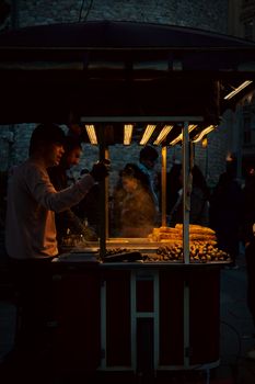 Captured during twilight, a street vendor prepares traditional snacks under glowing lights, creating a warm atmosphere.