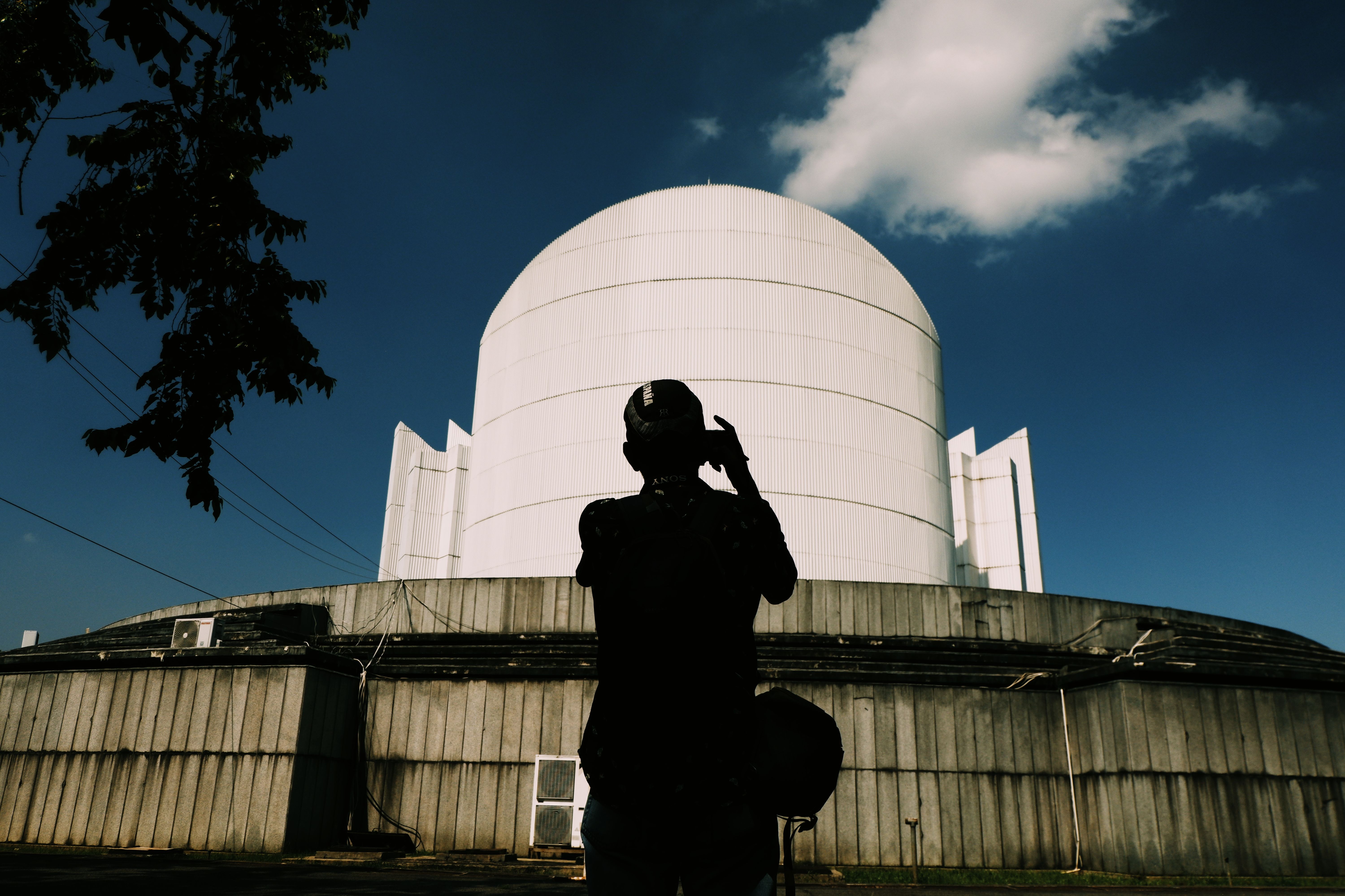 Silhouette of a man capturing a large white dome under a clear sky in Bandung.