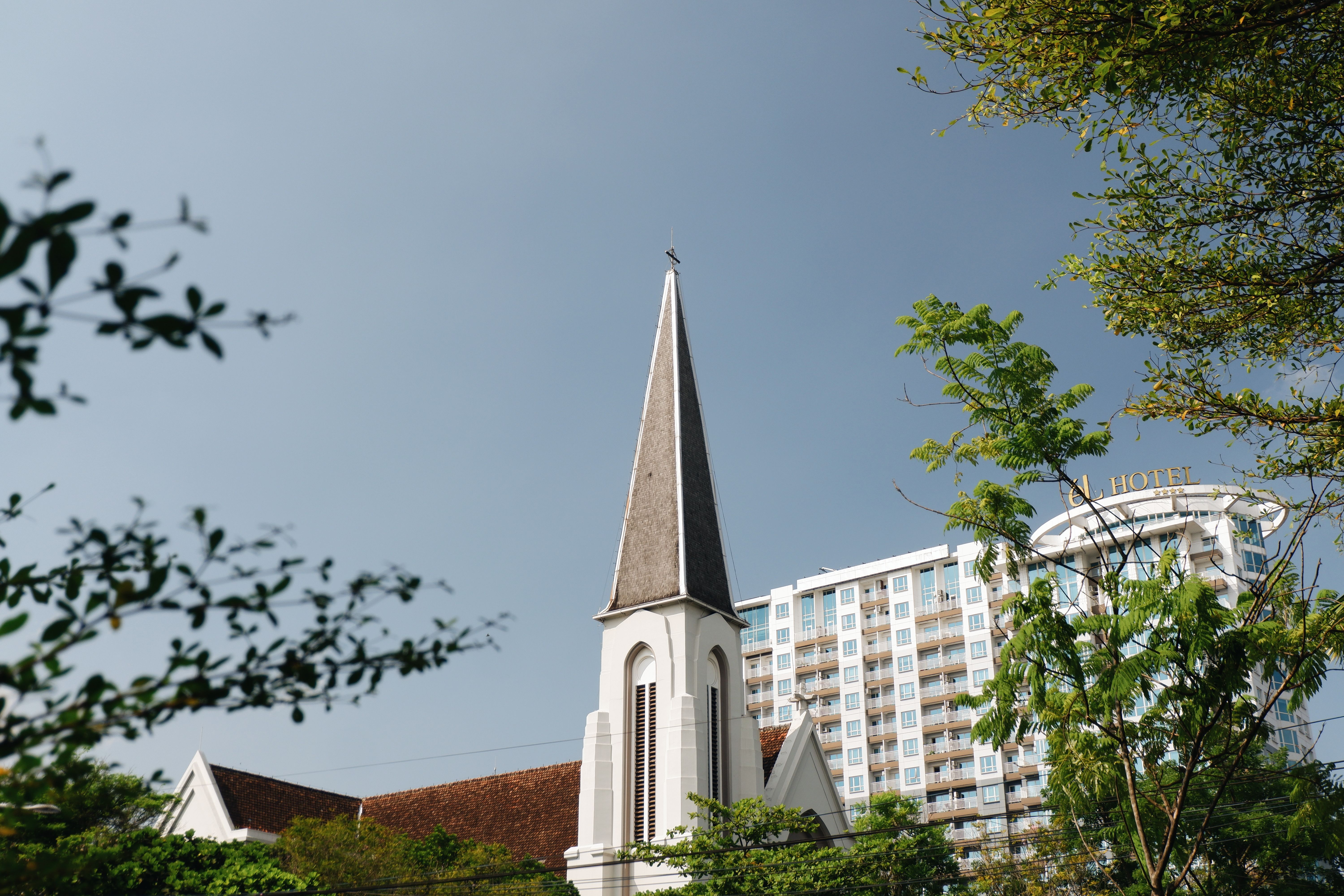 A historic church steeple amidst modern buildings in Bandung, Indonesia.