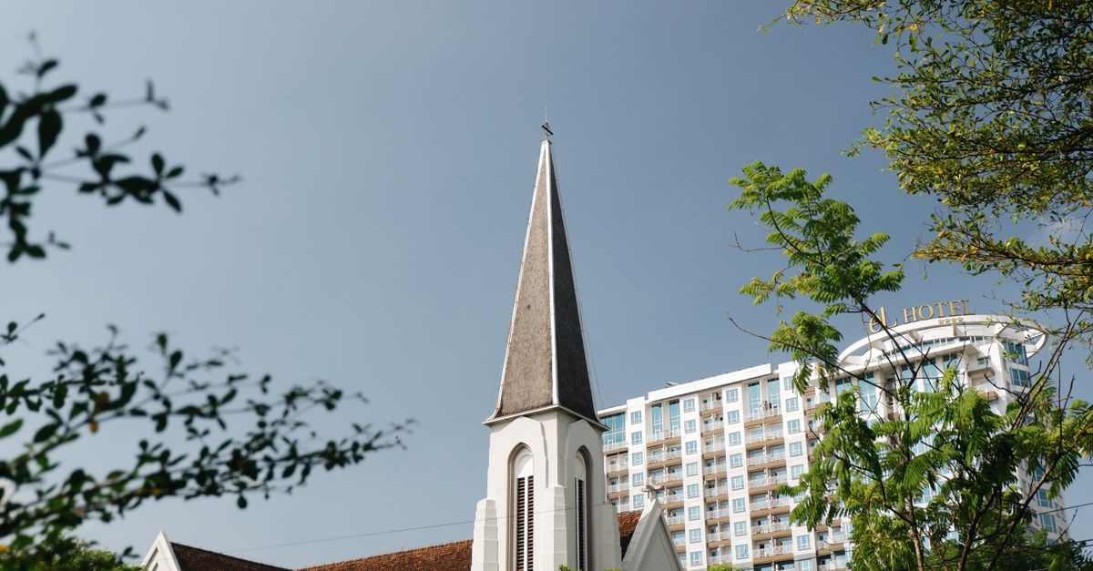 A historic church steeple amidst modern buildings in Bandung, Indonesia.