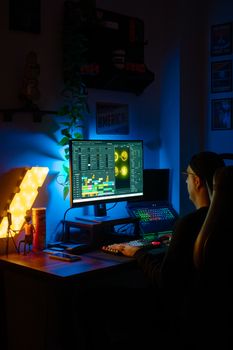 Focused individual at computer desk in neon-lit room, editing software open on screen.