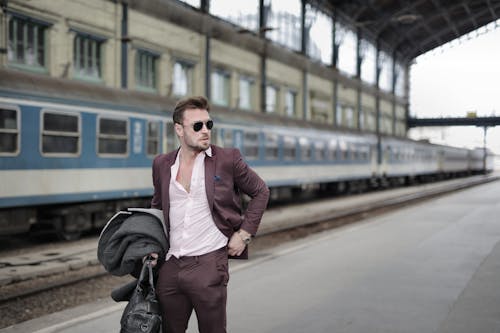 Fiducioso Viaggiatore Maschio Alla Moda In Piedi Sulla Piattaforma Della Ferrovia Con Cappotto E Borsa Da Viaggio