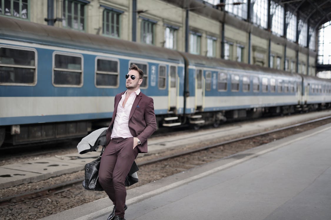 Man in Maroon Suit Walking on Sidewalk Beside Train