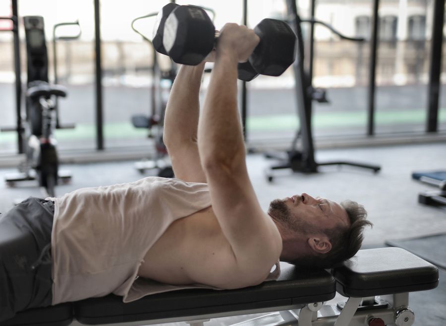 A member presses two dumbbells from a flat bench