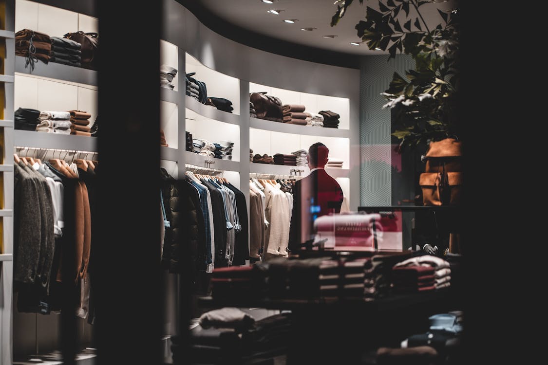 Back view of faceless elegant male customer in suit choosing new clothes while standing near wardrobe in modern fashion boutique