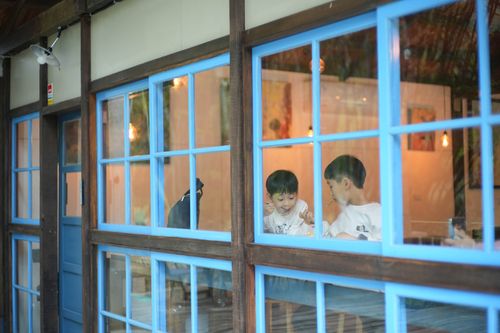 Free Two kids enjoying a meal inside a cozy cafe, seen through blue-framed windows. Stock Photo