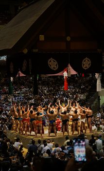 A group of sumo wrestlers perform a ritual dance during a traditional sumo tournament inside a Japanese arena.