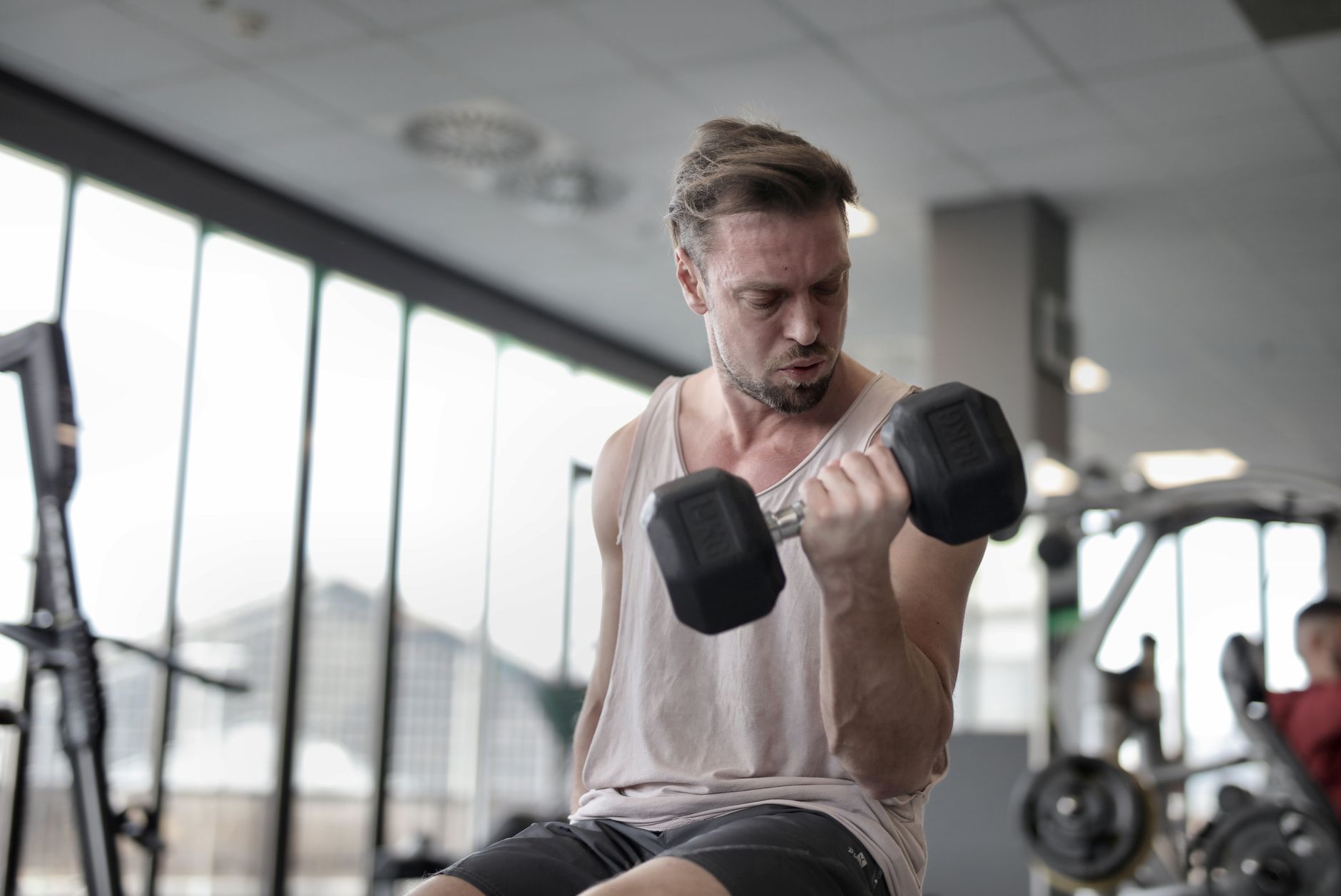 Adult man focused on lifting a dumbbell during a workout session in a gym.