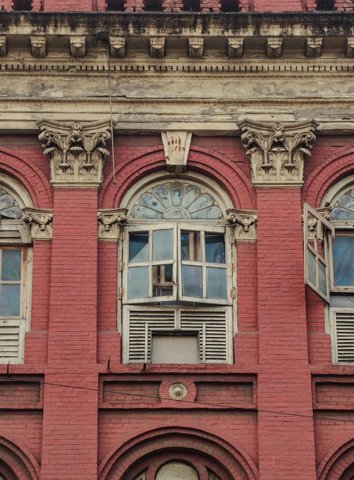 Free Close-up view of an old red brick building facade featuring ornate arched windows and detailed architecture. Stock Photo