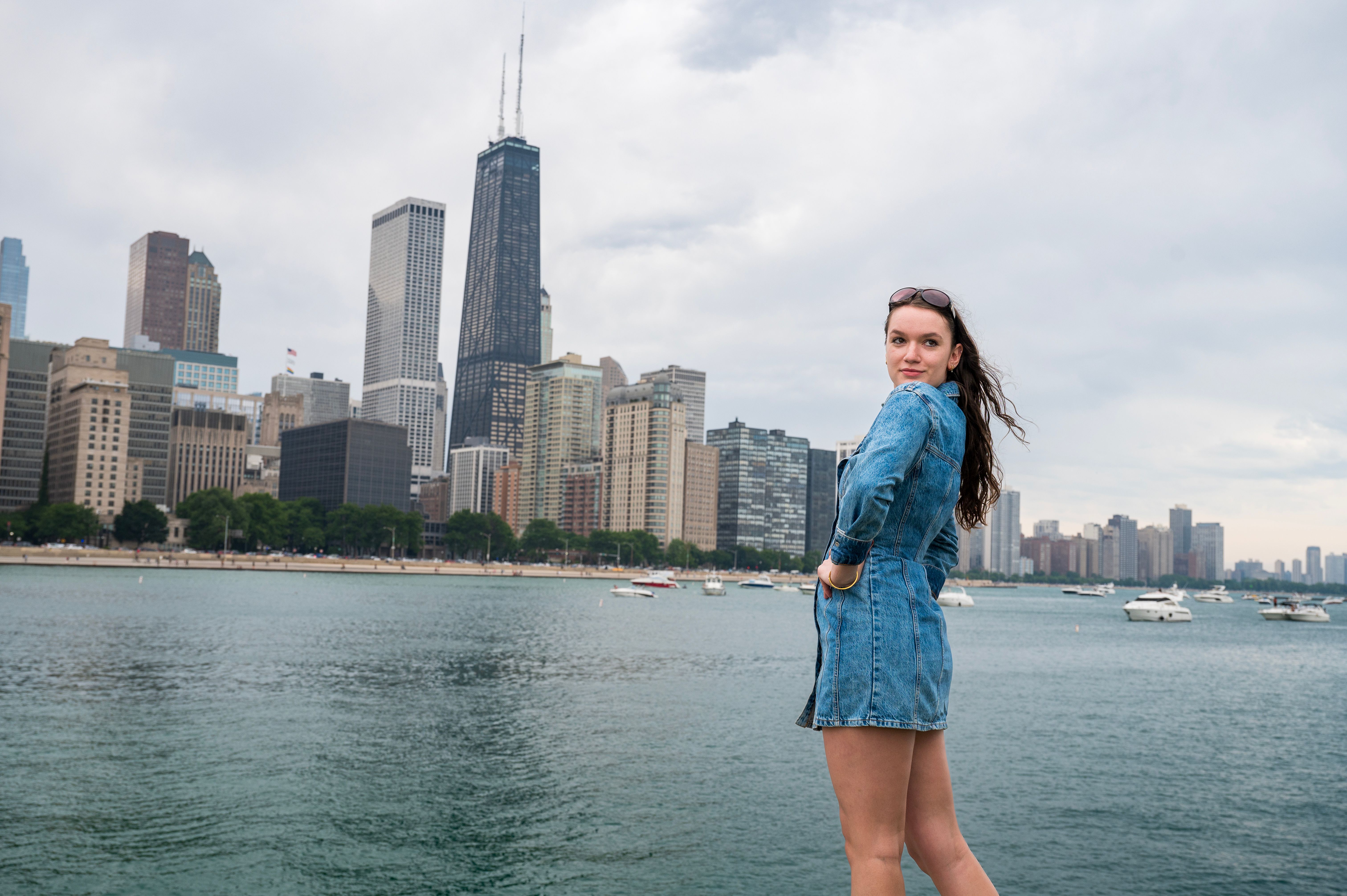 A woman standing by the waterfront with Chicago's skyline and John Hancock Center in the background.